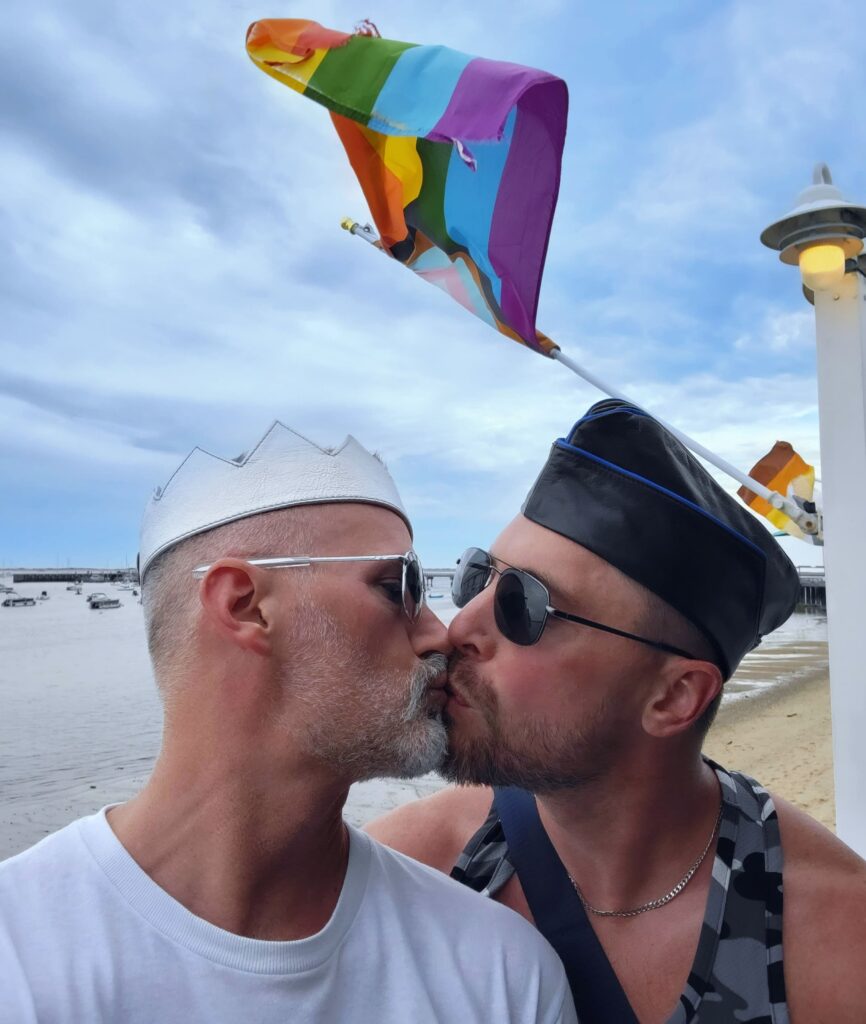 2 men kissing with a rainbow flag waving behind them