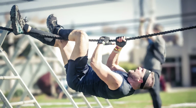 A muddy man doing a rope climb